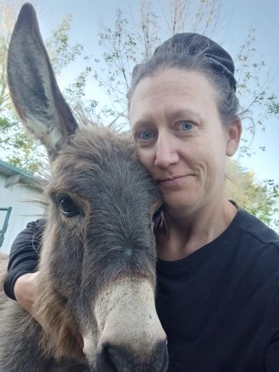 Woman gently hugging a donkey outdoors, both close to the camera.