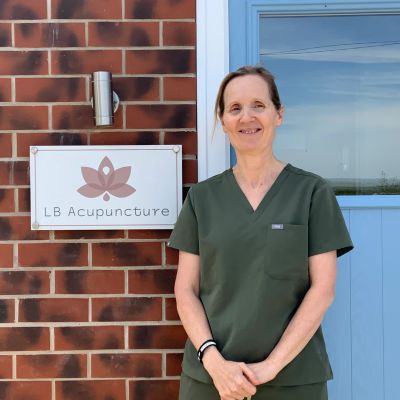Lisa Boudewijns in green scrubs standing by an acupuncture clinic sign
