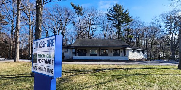 Real estate office with a sign for CITY2SHORE and Michigan Mortgage on a sunny day.