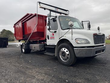 Ameritex hooklift truck hauling red roll-off dumpster container on gravel lot. Truck Right