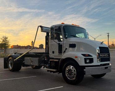 White Mack hooklift truck parked outdoors at sunset, built for roll-off hauling.