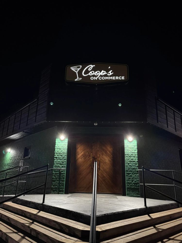 Entrance of Coop's on Commerce bar at night with illuminated sign and wooden doors.