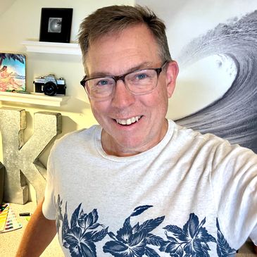 Smiling man in glasses wearing a floral print white t-shirt indoors.