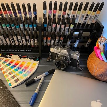 A creative workspace with markers, a vintage camera, and a laptop.