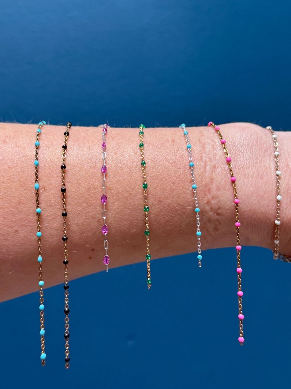 Seven delicate beaded bracelets on a wrist.