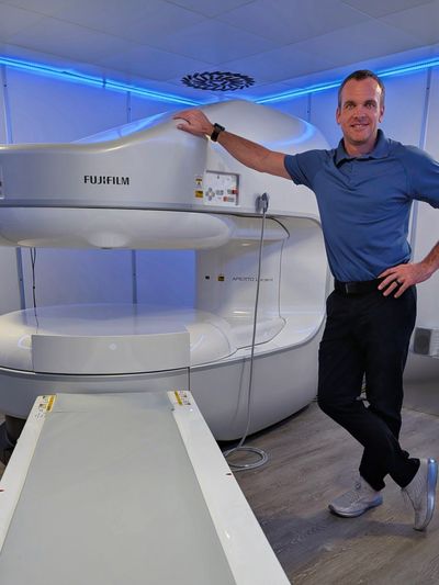 Man standing beside a Fujifilm MRI scanner in a modern medical room.