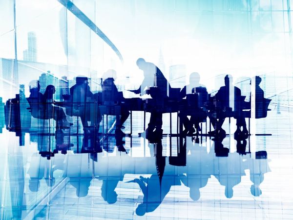 Silhouettes of people in a modern office meeting with cityscape reflections.
