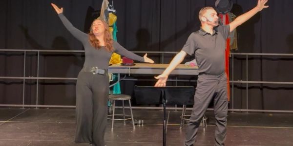 Two performers in black on stage with arms outstretched.