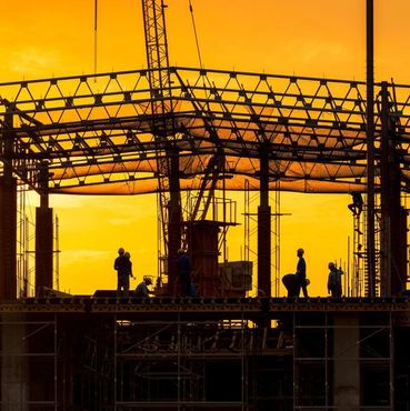 Silhouettes of construction workers at a building site during sunset.