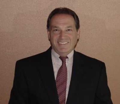Man in suit smiling against brown background.
