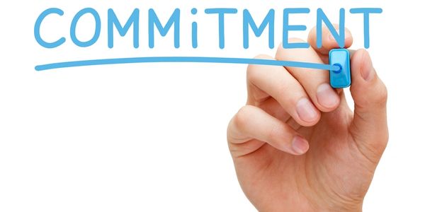A hand, using a pen to write the word commitment on glass.