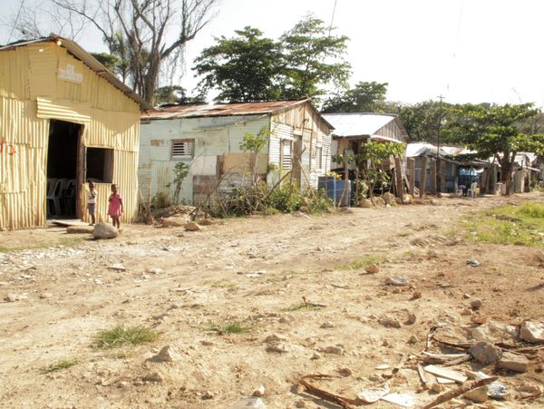 Rustic homes line a dusty road in a rural village under bright sunlight.