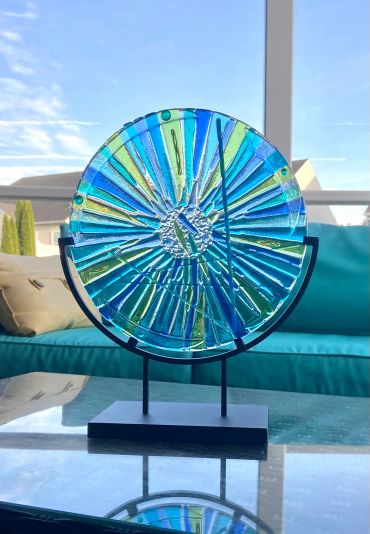 Colorful glass sundial on a stand with blue sky background.