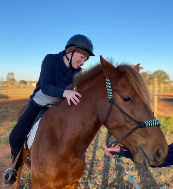 Young child happily riding a brown horse on a sunny day.