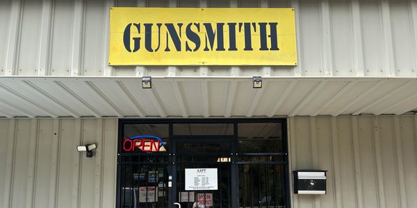 Front entrance of a gunsmith shop with a yellow sign.