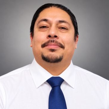 Man wearing white shirt and blue tie smiling slightly.