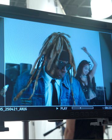 Monitor shows a man with dreadlocks and sunglasses, woman dancing in background.