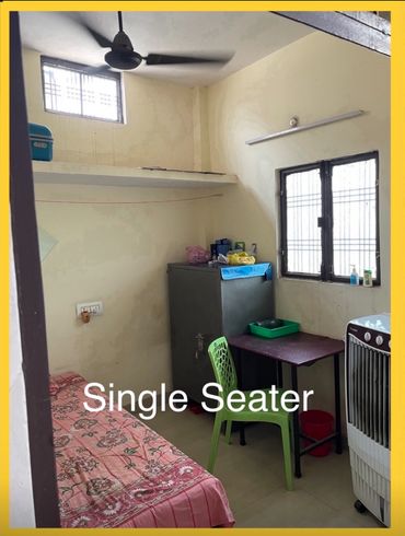 A simple single seater room with basic furniture and a fan.