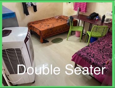 Simple double-seater room with two beds and green chairs.