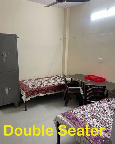 A simple double seater room with two beds and a table.