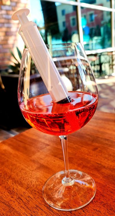 Wine glass with red liquid and cocktail syringe