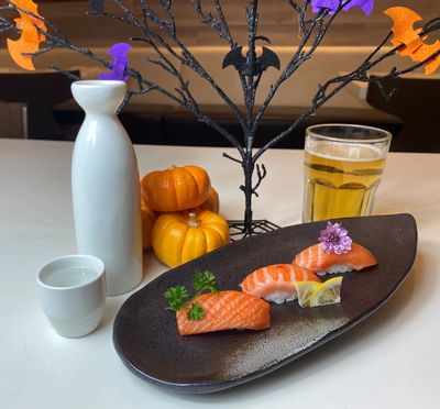 Plate of sushi with mini Halloween tree decorated with bats. Glass of beer and caraf of sake