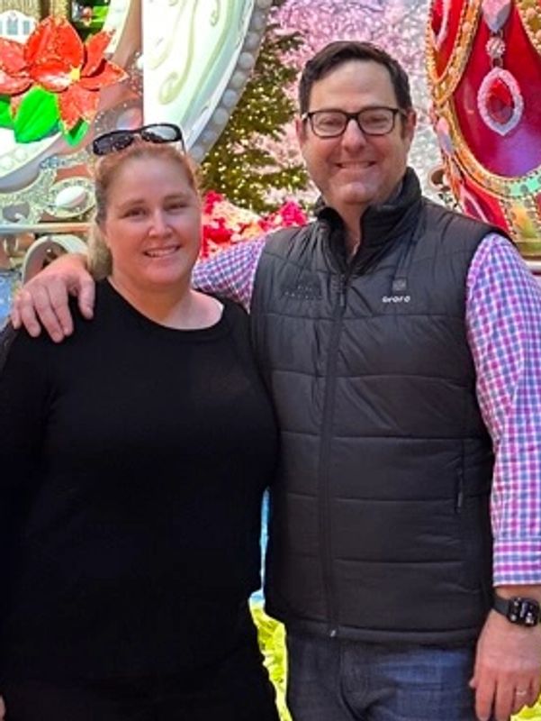 Two people smiling outdoors with colorful background.