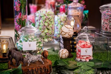 Decorative candy jars and animal figurines on a vibrant jungle-themed table.