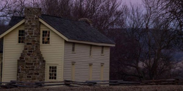 A rustic house with a stone chimney at dusk.