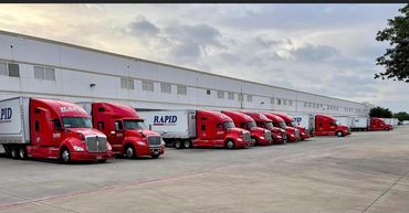 Row of red semi trucks parked at a warehouse.