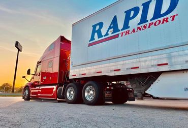 Red semi-truck parked under a sunset sky.