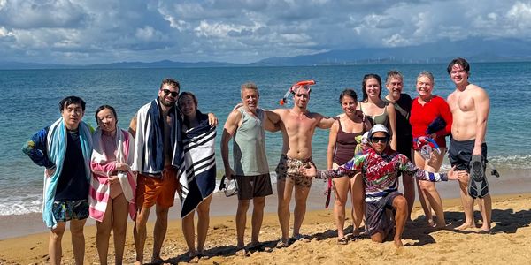 Group of friends posing on a beach with towels and swimwear.