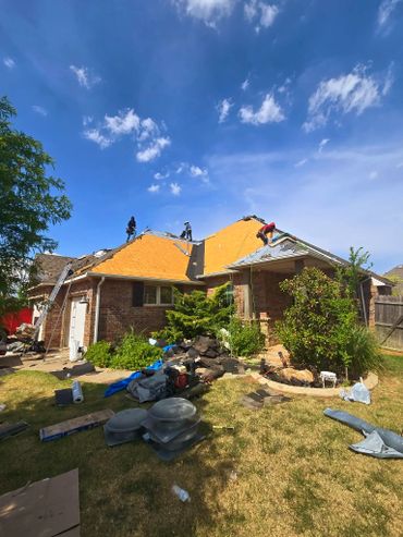 Workers installing a new roof on a brick house under clear blue sky.