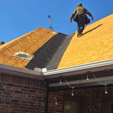 Worker installing roofing underlayment on a steep roof under clear blue sky.