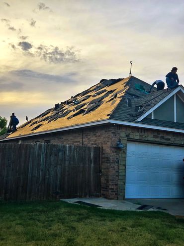 Workers replacing shingles on a house roof during sunset.