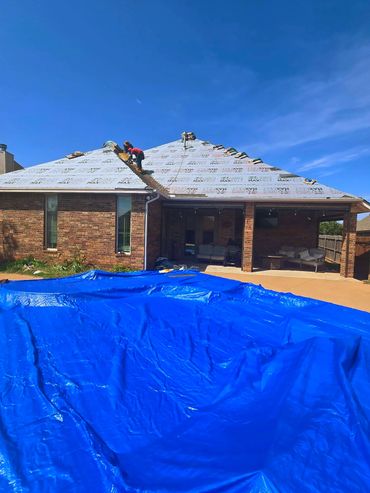 Workers are installing roofing underlayment on a house on a sunny day.
