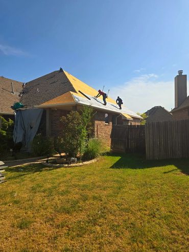 Two workers repairing a house roof under clear blue sky.