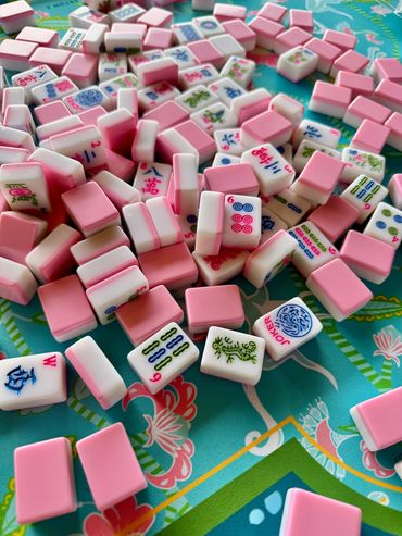 Pink and white Mahjong tiles scattered on a colorful surface.