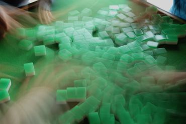 Blurred hands rapidly arranging green Mahjong tiles on a green table.