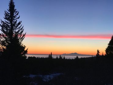 Sunset over a forest with a mountain silhouette and vibrant sky colors.