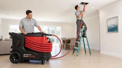 Two Airsource technicians cleaning a ceiling duct with a BrushBeast DR in a Southwest Florida home