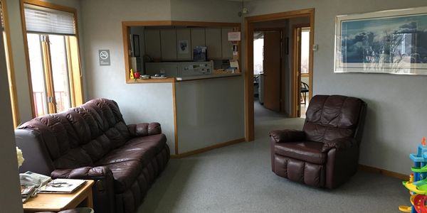 View of office waiting room from front door, shows recliner, couch, and front desk area. 