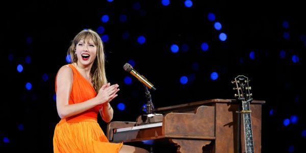 Woman in orange dress clapping by a piano on stage.