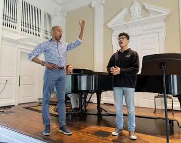 Two men singing with piano accompaniment in a recital room.
