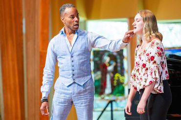 A man teaching a young woman to sing in a music studio.