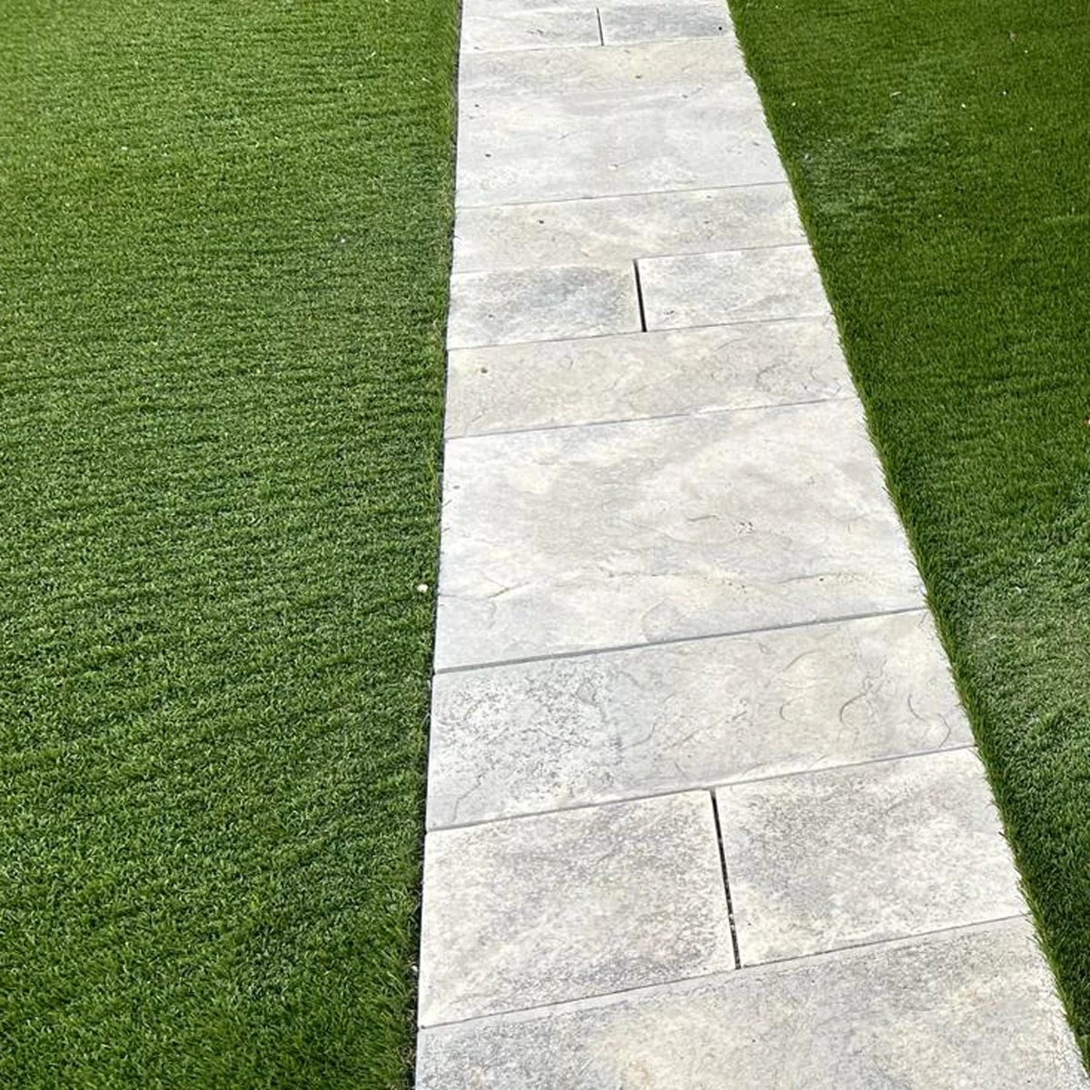 Stone pathway between two strips of green grass beside a white wall.