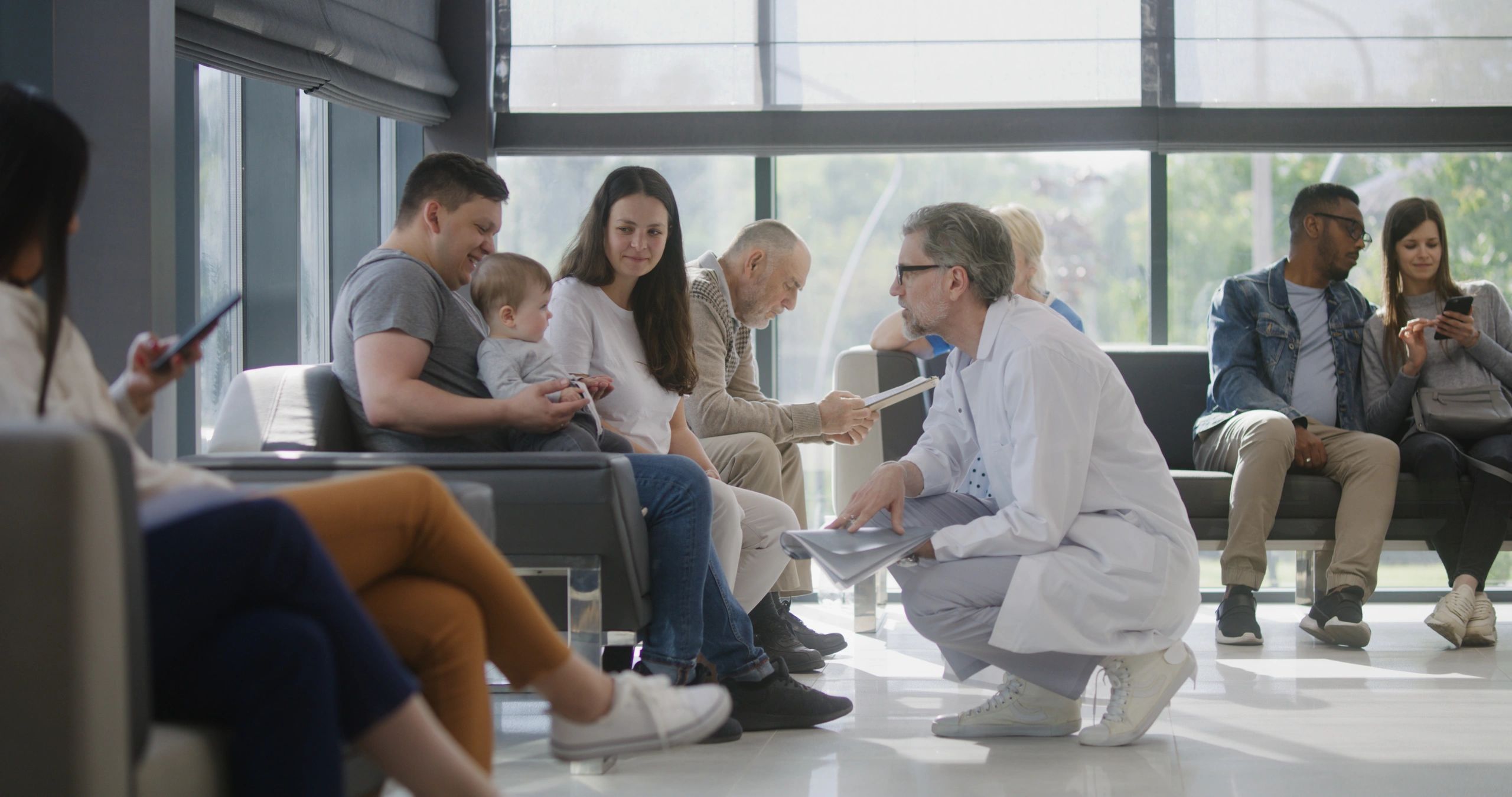 Waiting room with diverse people and a doctor consulting a family with a baby.