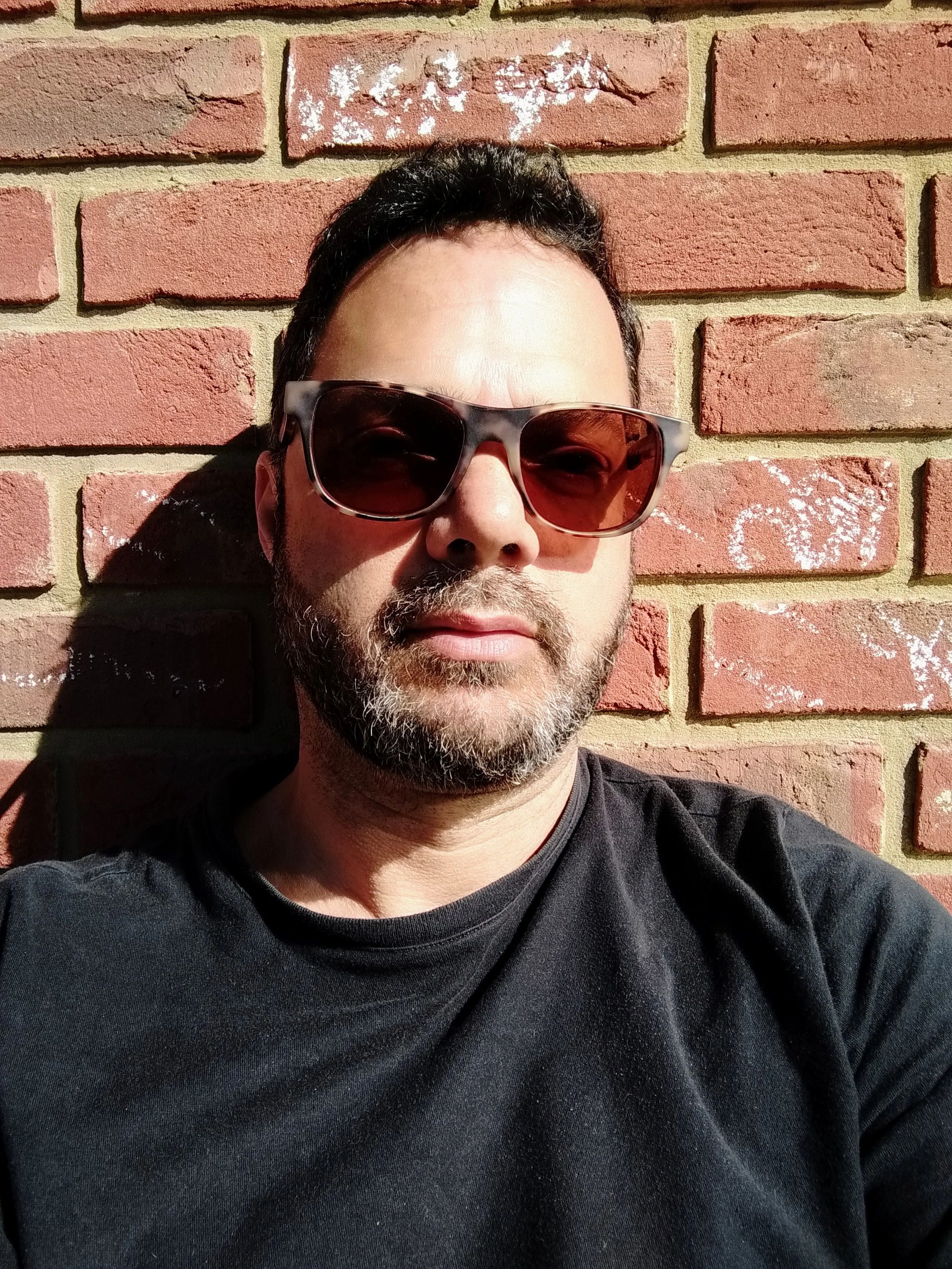 Karim Ahmed in glasses and black T-shirt against brick wall