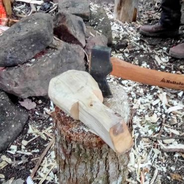 A rustic axe and wood carving near a campfire.