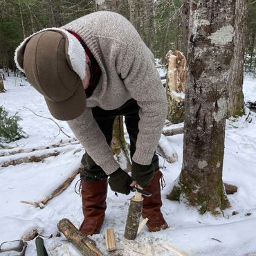 Person whittling wood in snowy forest.